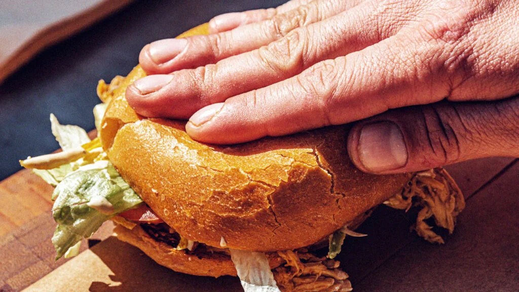 A hand pressing on a hamburger, a typical comfort food