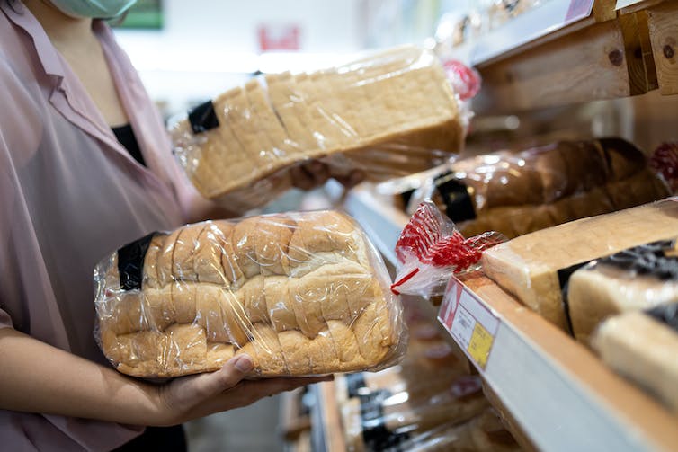 A woman is holding two loaves of bread from the supermarket.